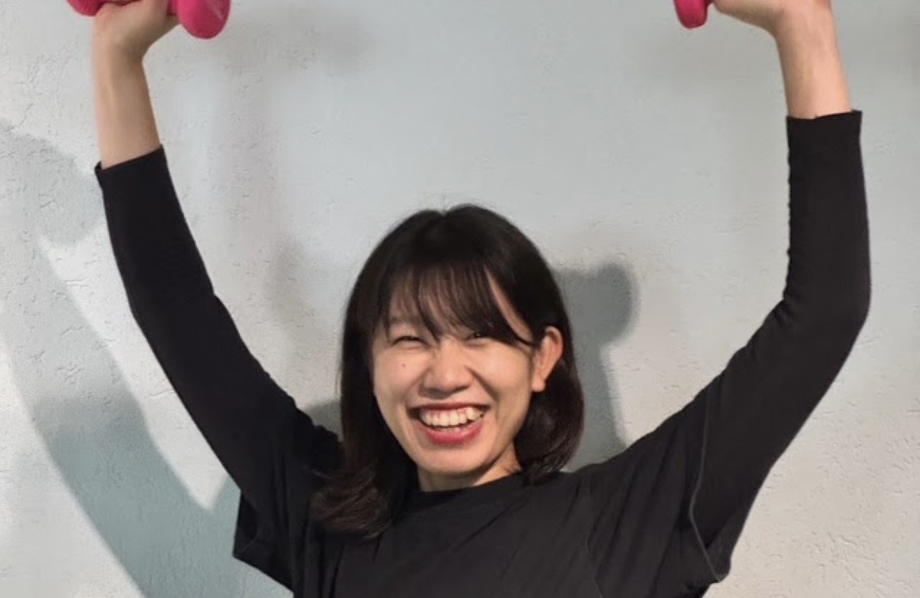 Risei Ando smiling while holding dumbbells overhead